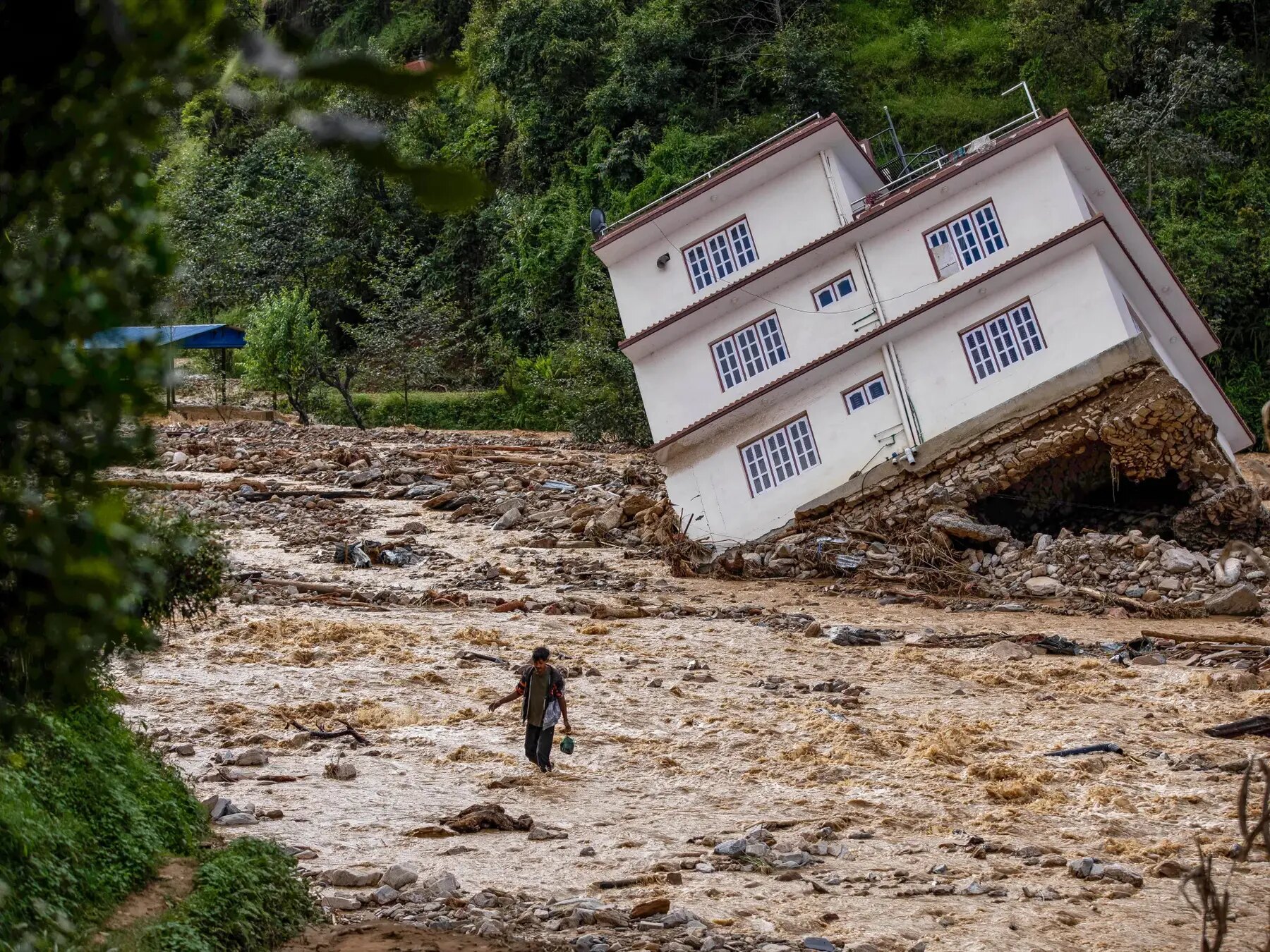 A damaged house leaning over floodwater and debris in Nepal